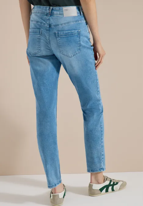 Mid Waist Slim Leg Jeans im Casual Fit light blue wash Rückansicht einer Person in hellblauen Jeans und weißen Sneakern mit grünen Details.