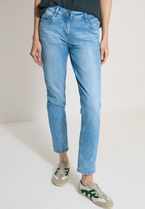 Mid Waist Slim Leg Jeans im Casual Fit light blue wash Eine Person trägt schmale hellblaue Jeans und grün-weiße Sneaker, Oberteil in Schwarz.