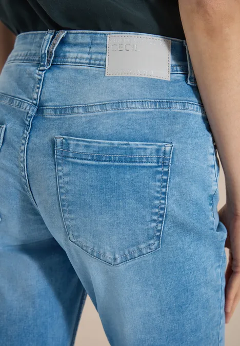 Mid Waist Slim Leg Jeans im Casual Fit light blue wash Frau von hinten in hellblauen Jeans mit Gesäßtasche und weißem Label, schwarzes Oberteil.