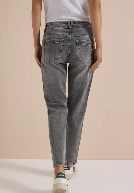 Mid Waist Slim Leg Jeans im Casual Fit light grey wash Eine Person von hinten trägt graue Jeans und weiße Sneaker vor hellem Hintergrund.