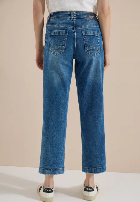 Achteraanzicht van een persoon in rechte, enkelhoge blauwe jeans en witte espadrilles.