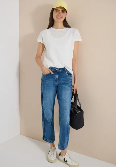 Vrouw in los wit T-shirt, blauwe high waist jeans, witte sneakers en een zwarte stoffen tas.