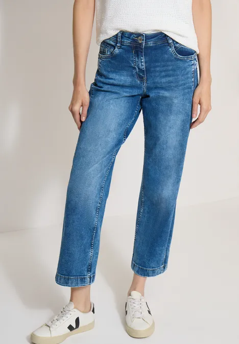 Een persoon draagt een rechte blauwe jeans en witte sneakers.