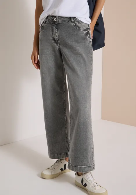High Waist Wide Leg Jeans im Loose Fit light grey wash Ein Model trägt weite, graue High-Waist-Jeans und weiße Sneaker.