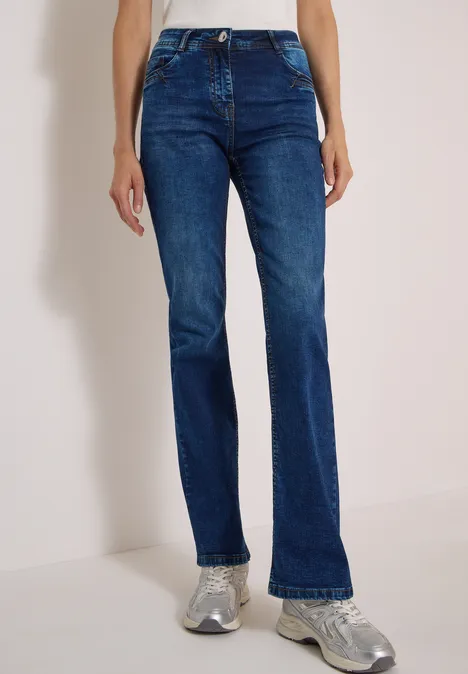 High Waist Bootcut Jeans im Slim Fit mid blue used wash Eine Person trägt dunkelblaue gerade Jeans und graue Sneaker vor hellem Hintergrund.