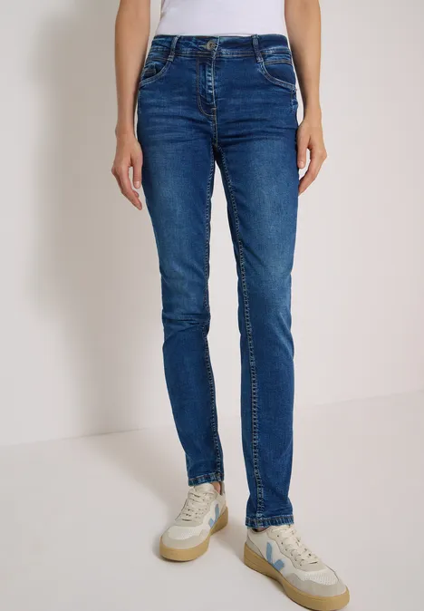 Mid Waist Slim Leg Jeans w stylu Casual Fit mid blue used wash Osoba nosi obcisłe niebieskie dżinsy i białe trampki.