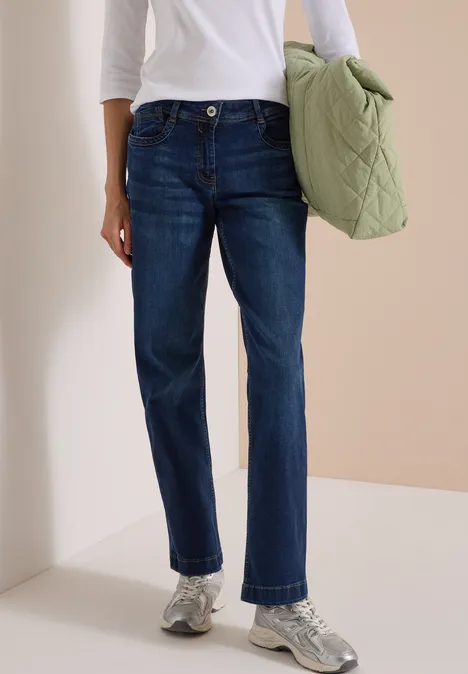 High Waist Wide Leg Jeans w kroju Loose Fit Dark blue wash Osoba ma ciemne, proste dżinsy, biały top, srebrne buty sportowe i trzyma zieloną pikowaną torbę.