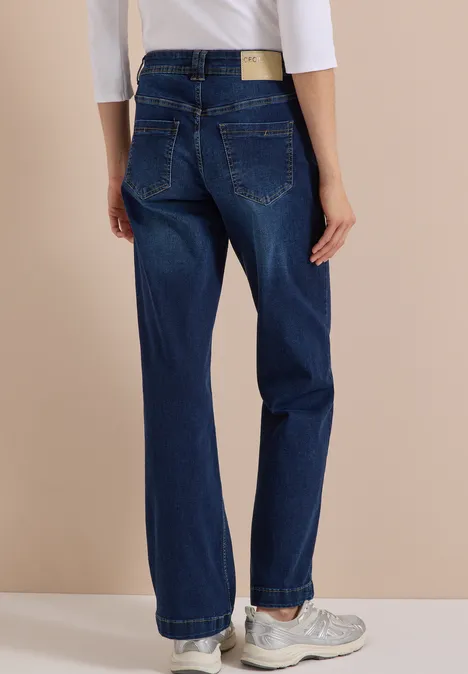 High Waist Wide Leg Jeans w kroju Loose Fit Dark blue wash Widok z tyłu osoby w ciemnoniebieskich, szerokich dżinsach i białych trampkach na beżowym tle.