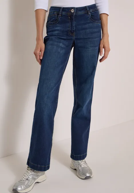 High Waist Wide Leg Jeans w kroju Loose Fit Dark blue wash Kobieta w szerokich ciemnoniebieskich dżinsach i srebrnych trampkach na neutralnym tle.