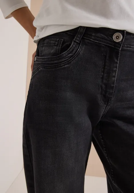 Eine Person trägt schwarze Jeans mit sichtbarem Knopf und weißem Shirt, nur Taille und Hüfte sichtbar.