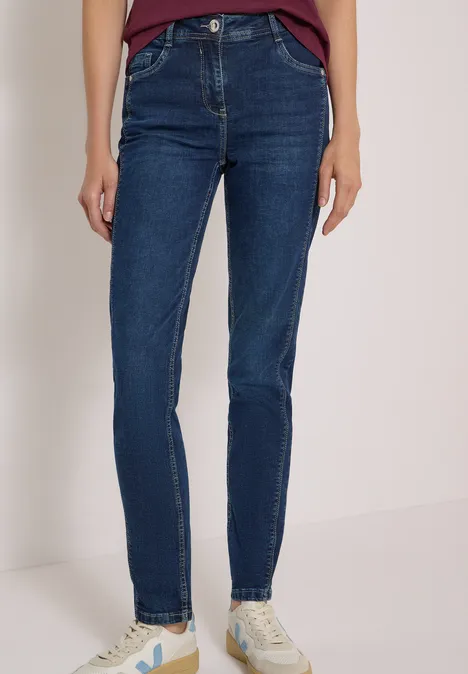 Person in dunklen Skinny-Jeans und weißen Sneakern, nur Beine und Füße sind zu sehen.