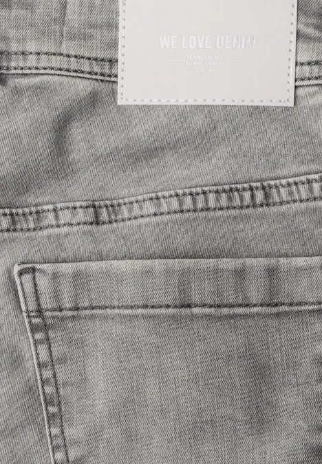 High Waist Bootcut Jeans im Slim Fit light grey wash Ausschnitt einer grauen Jeansrückseite mit Gesäßtasche, Gürtelschlaufen und Etikett „WE LOVE DENIM“.