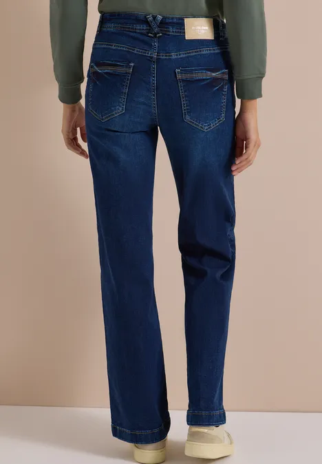 Achteraanzicht: damesjeans donkerblauw met rechte pijpen, achterzakken en witte sneakers.