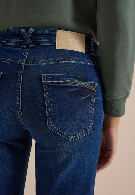 Een persoon draagt donkerblauwe jeans en een groene trui, gezien van achteren.