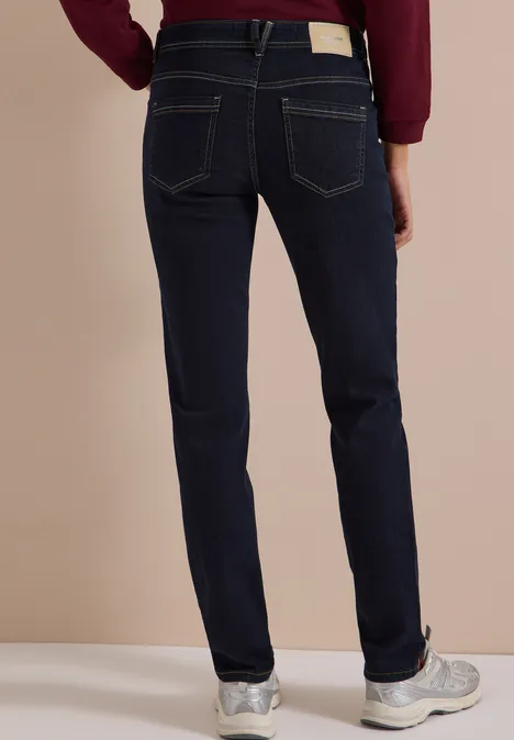 Mid Waist Slim Leg Jeans im Casual Fit rinsed wash Rückenansicht einer Person in dunkelblauen Jeans und weißen Sneakern.