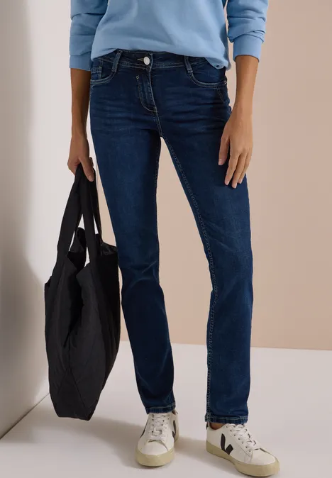 Persoon met donkerblauwe jeans, witte sneakers en lichtblauw shirt, draagt een zwarte tas.