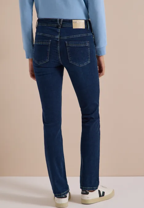 Achteraanzicht van persoon in donkerblauwe rechte jeans en witte sneakers voor neutrale achtergrond.