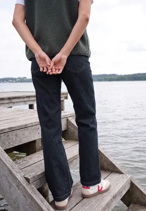 High Waist Wide Leg Jeans im Loose Fit rinsed wash Person steht in Jeans und Sneakers auf einer Holztreppe am See, Hände hinter dem Rücken verschränkt.