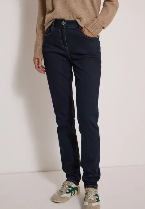 Person trägt dunkelblaue Jeans, beigen Sneaker und braunen Pullover in schlichtem Stil.