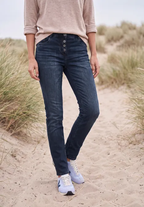 Jeans met Mid Waist-taille en Slim Leg-pijpen in casual pasvorm blue black used wash Persoon met blauwe spijkerbroek en licht trui loopt op een zandig duinpad met helmgras.