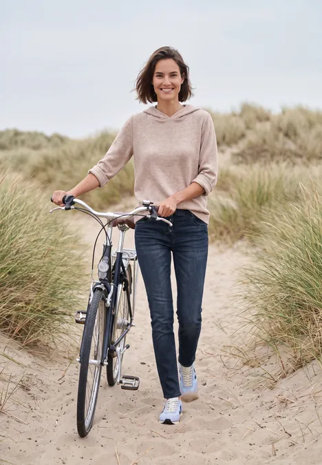 Jeans met Mid Waist-taille en Slim Leg-pijpen in casual pasvorm blue black used wash Een lachende vrouw loopt met haar fiets over een zandig duinenpad, omringd door helmgras.