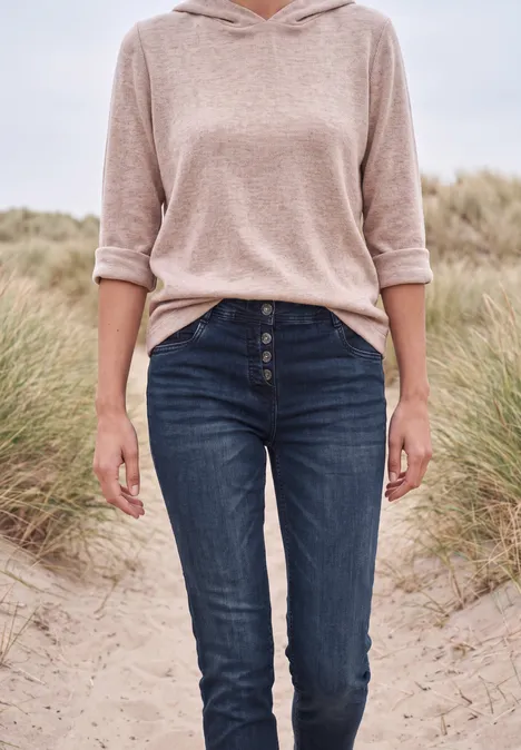Jeans met Mid Waist-taille en Slim Leg-pijpen in casual pasvorm blue black used wash Een vrouw in een beige hoodie en blauwe jeans staand op een strand met duinen.