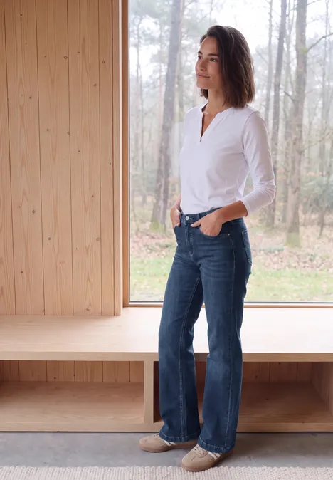Wide Leg Jeans mit Gallonstreifen mid blue used wash Frau im weißen Hemd und weiten Jeans steht seitlich in einem hellen Holzraum vor einem Fenster mit Waldblick.