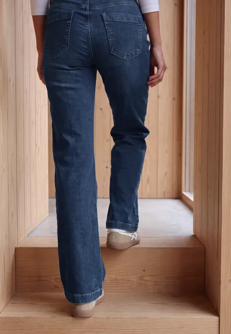 Wide Leg Jeans mit Gallonstreifen mid blue used wash Person in Jeans steigt eine helle Holztreppe hinauf, Rückenansicht bis zur Taille sichtbar.