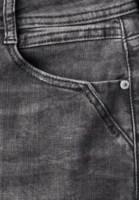 Gros plan sur un jean foncé montrant une poche arrière, des coutures et un rivet.