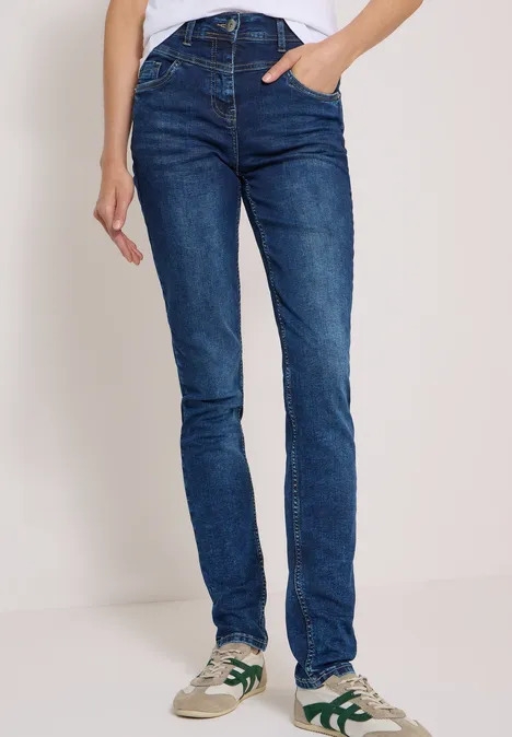 Persoon draagt strakke blauwe jeans en witte sneakers met groene accenten.