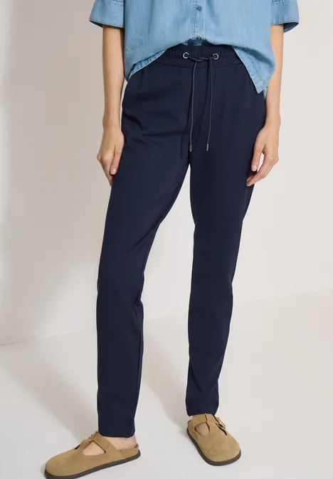 Mid Waist Slim Leg Hose in casual pasvorm urban dark blue Een persoon draagt donkerblauwe, comfortabele broek met koord en beige instappers.