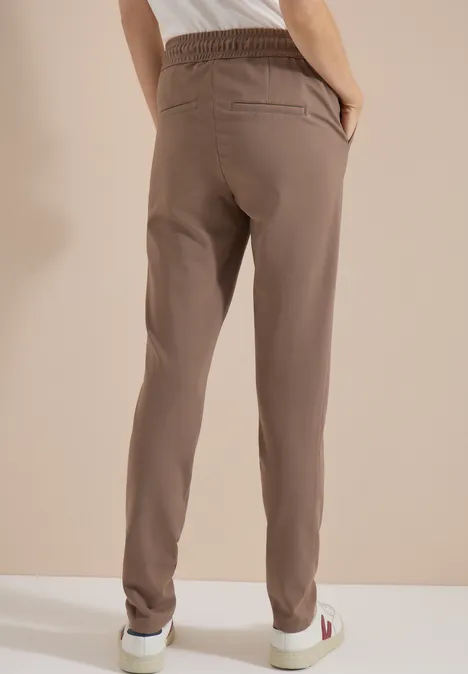 Achteraanzicht van een persoon in beige sweatbroek en witte sneakers tegen neutrale achtergrond.
