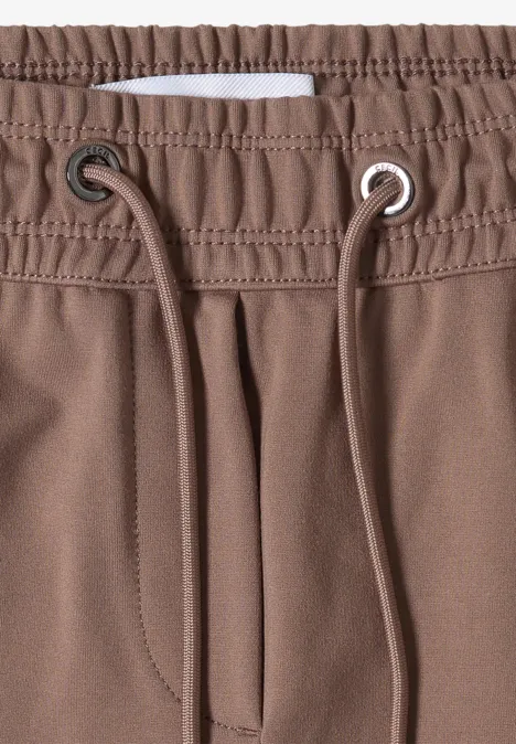 Close-up van een bruine broek met elastische taille, aantrekkoord, metalen oogjes en zichtbare stiksels.