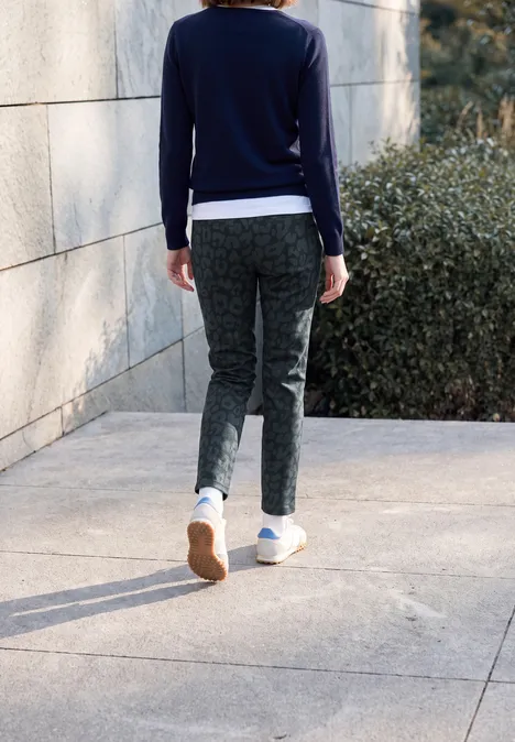 Vue arrière d’une personne portant un haut bleu foncé, un pantalon gris et des baskets blanches sur un chemin en pierre.