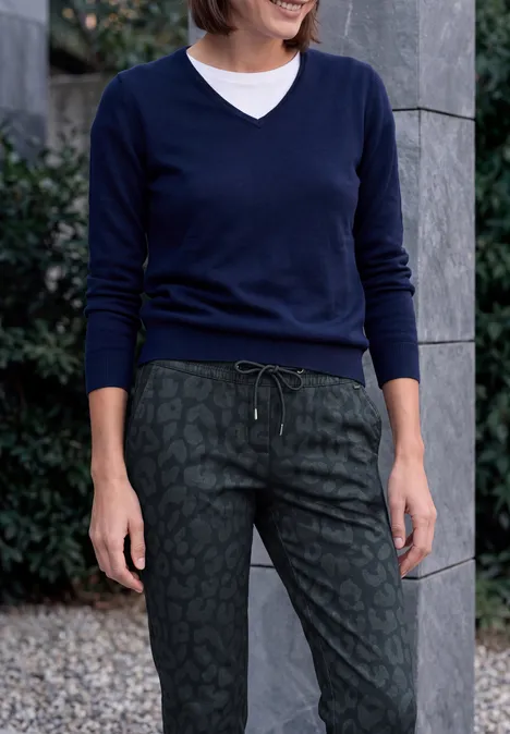 Femme en pull bleu marine à col V sur T-shirt blanc et pantalon vert imprimé léopard avec cordon, debout dehors.