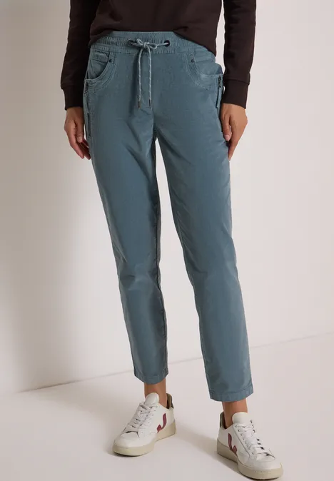Mid Waist Slim Leg Hose im Casual Fit dove blue Frau trägt smaragdgrüne Chinohose mit Kordelzug, kombiniert mit weißen Sneakern.