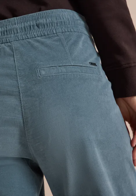 Mid Waist Slim Leg Hose im Casual Fit dove blue Rückansicht einer Person in hellblauen Cordhosen und schwarzem Oberteil, Fokus auf Gesäßtasche