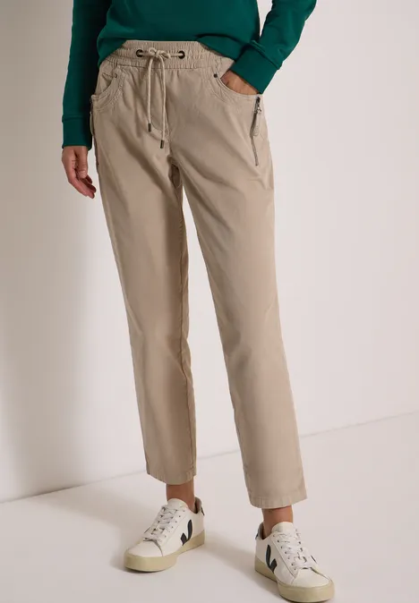 Mid Waist Slim Leg Hose im Casual Fit silvery beige Model trägt beige Hose mit Kordelzugbund, seitlichen Taschen und weißen Sneakern, lässiger Look.