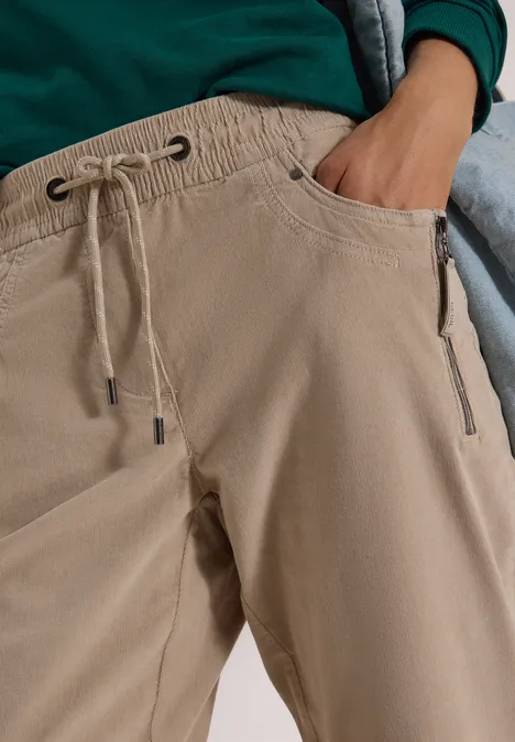 Mid Waist Slim Leg Hose im Casual Fit silvery beige Nahaufnahme einer Person in beigen Hosen mit Tunnelzug und Taschen, Hand in der Tasche.