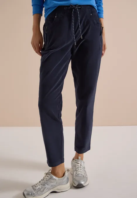 Mid Waist Slim Leg Hose im Casual Fit dark blue corduroy Eine Person trägt dunkelblaue Jogginghose mit Bündchen und silbergraue Sneakers vor hellem Hintergrund.