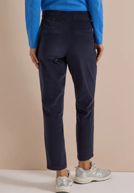Mid Waist Slim Leg Hose im Casual Fit dark blue corduroy Eine Person steht von hinten, trägt eine marineblaue Cordhose, blauen Pullover und weiße Sneaker.