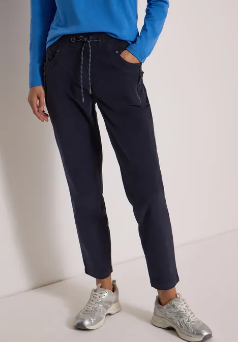 Mid Waist Slim Leg Hose im Casual Fit dark blue corduroy Modell in dunkelblauer Freizeithose mit Kordelzug und silbernen Sneakern vor neutralem Hintergrund.