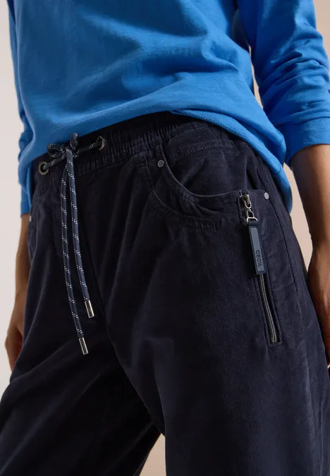 Mid Waist Slim Leg Hose im Casual Fit dark blue corduroy Dunkelblaue Cord-Jogginghose mit Kordelzug und Reißverschlusstaschen, kombiniert mit blauem Shirt.