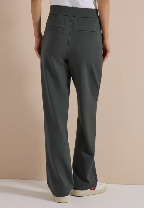 Frau trägt weite, gerade, dunkelgraue Hose im minimalistischen Stil, Rückansicht.