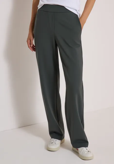 Dunkelgrüne, weite Damenhose mit geradem Schnitt und seitlichen Taschen, kombiniert mit weißen Sneakers.