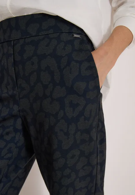 Nahaufnahme einer dunklen, leopardenmusternden Hose mit seitlicher Tasche und weißem Oberteil
