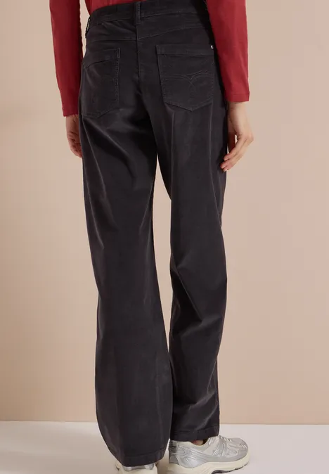 High Waist Wide Leg Hose im Loose Fit carbon grey Rückansicht einer Person in schwarzen, weiten Cordhosen und Turnschuhen vor beigem Hintergrund.