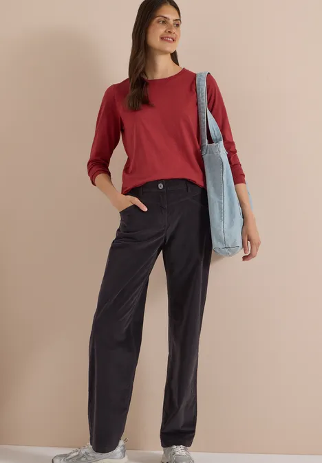 High Waist Wide Leg Hose im Loose Fit carbon grey Frau in rotem Pullover, weiten schwarzen Hosen und Stofftasche vor beigem Hintergrund.