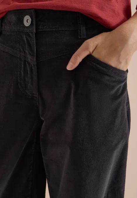 High Waist Wide Leg Hose im Loose Fit carbon grey Nahaufnahme einer Person mit rotem Oberteil und dunkler Cordhose, Hand in Seitentasche.
