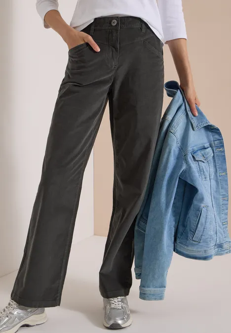 High Waist Wide Leg Hose im Loose Fit easy khaki Person trägt schwarze, weite Hose mit Taschen, weiße Bluse und silberne Sneaker, hält eine hellblaue Jeansjacke.